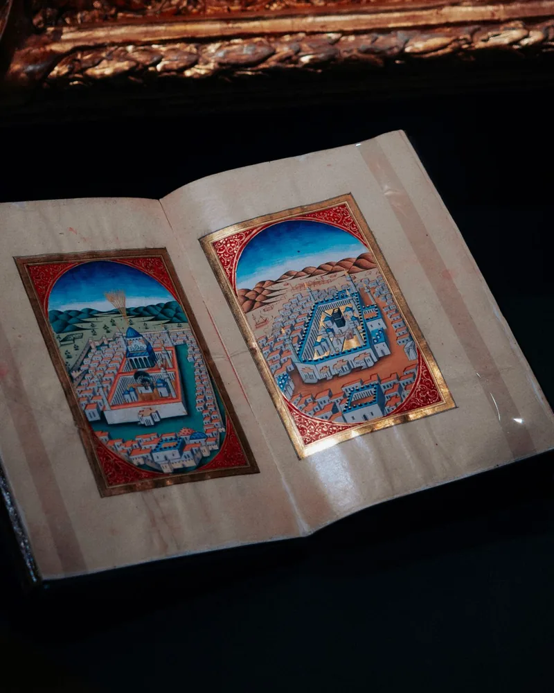 Manuscrito iluminado abierto con dos miniaturas enmarcadas en rojo y oro sobre fondo oscuro